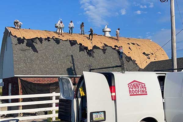 Sonntag Roofing team member on an arcing roof removing its old shingles with one of their work vans parked in front