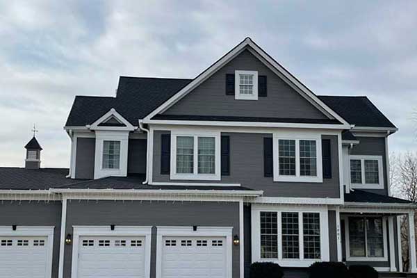 Front view of a large, two-story mid-class home with brand new black shingles and dark gray siding installed by Sonntag Roofing